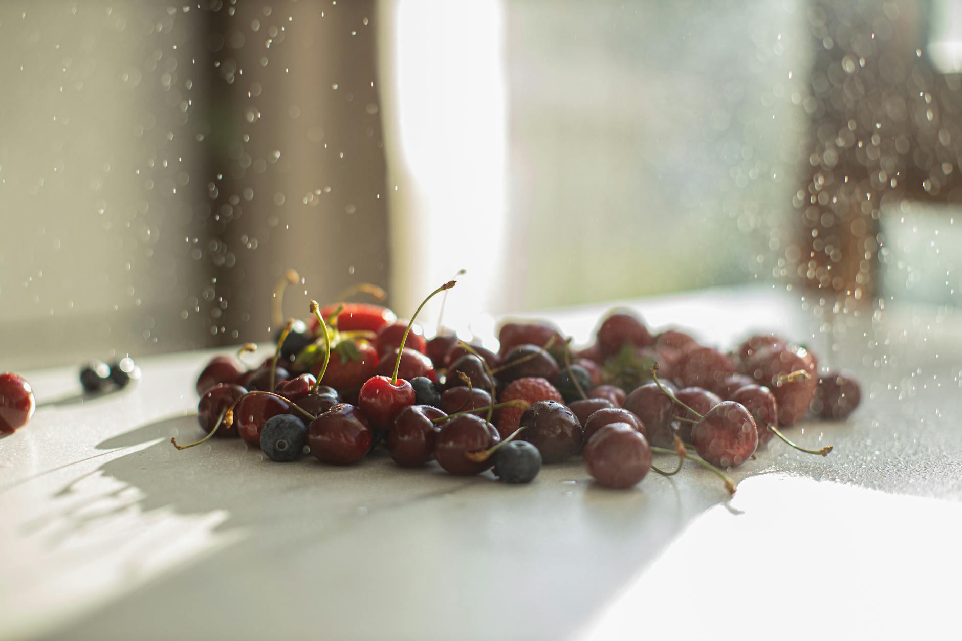 Un assortiment rafraîchissant de cerises et de bleuets avec des gouttelettes d'eau sur une table ensoleillée.